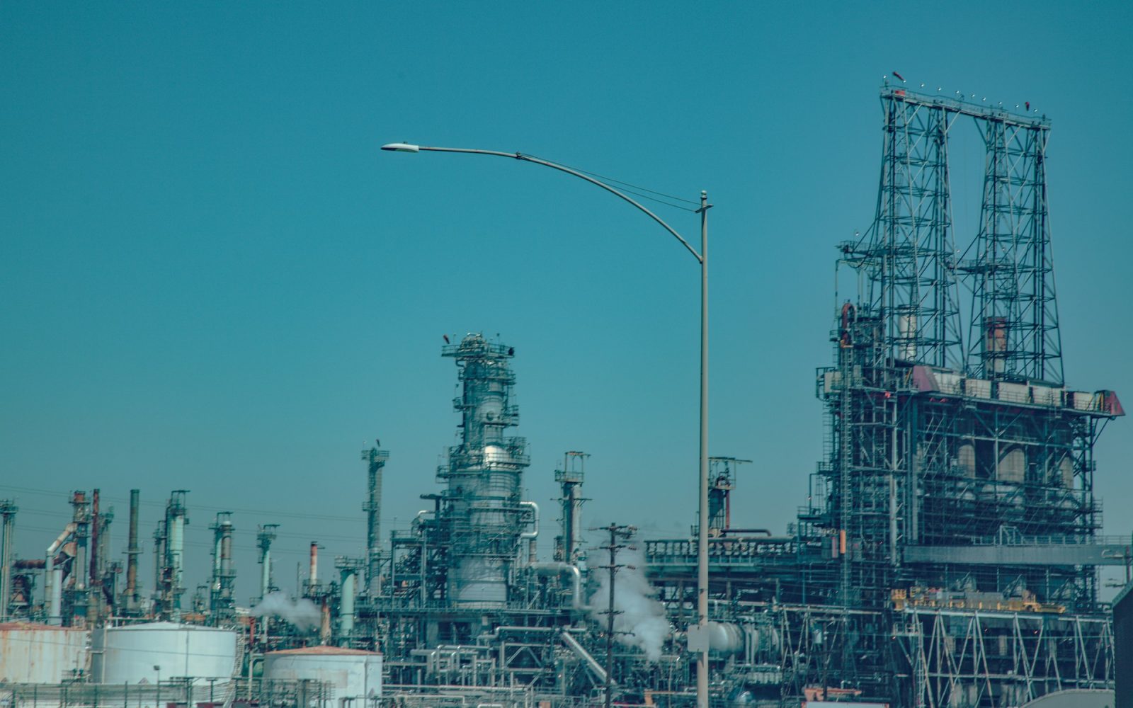 Refinery processing units and industrial pipework under a clear sky.